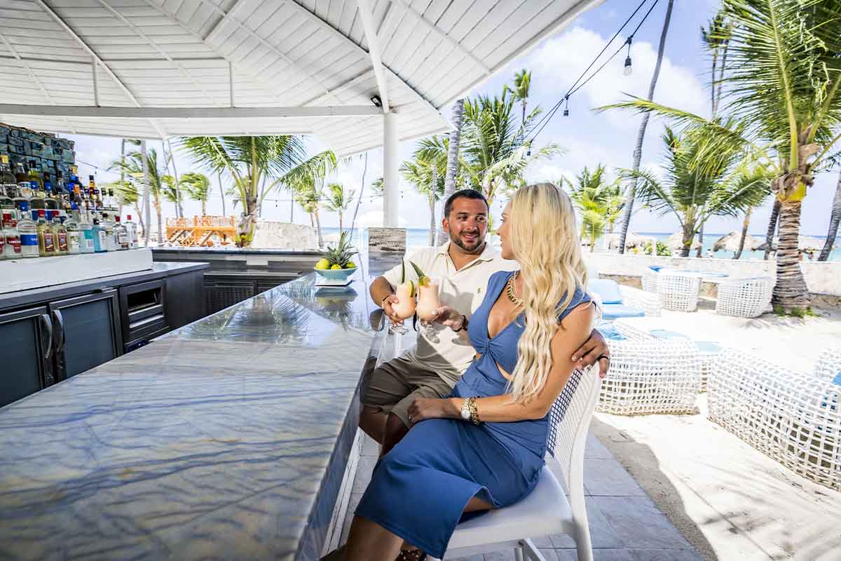 Pareja brindando con un cóctel en el bar exterior frente a la playa del Majestic Mirage Punta Cana