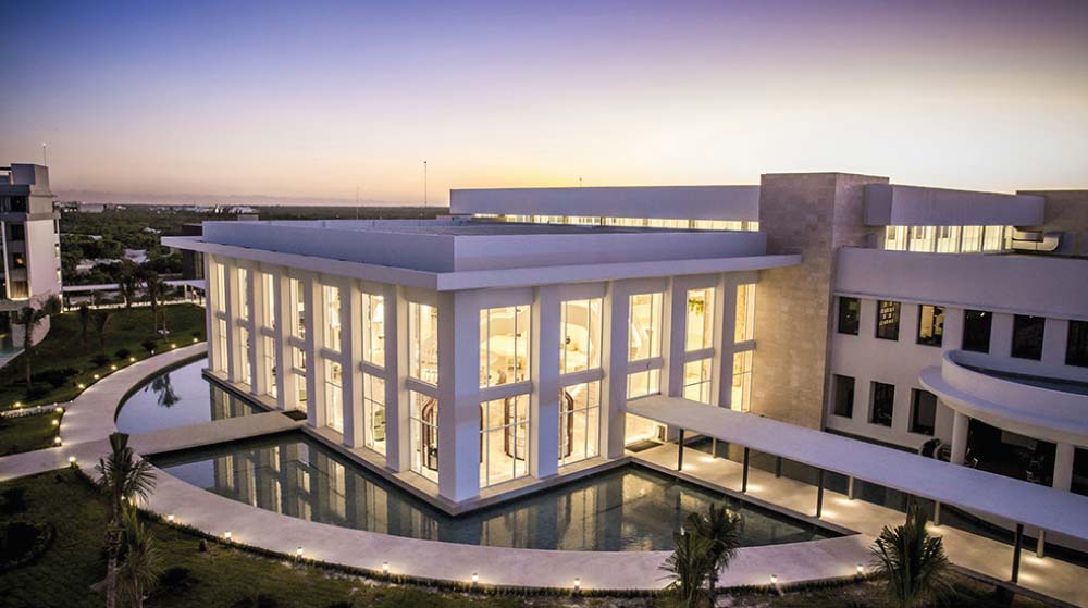 Edificio iluminado rodeado de una fuente al atardecer en Majestic Elegance Costa Mujeres